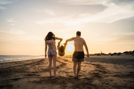 Téléchargez les photos : Jeune couple bronzer leur fils sur la plage, jouer dans la lumière du coucher du soleil - en image libre de droit
