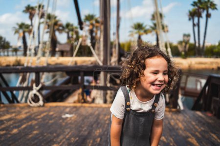 Téléchargez les photos : Portrait d'un petit garçon décontracté heureux et souriant debout sur un vieux bateau, faisant du tourisme en voyage - en image libre de droit