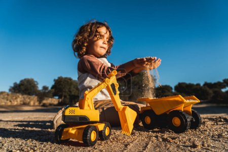 Photo for Nice happy little boy playing with excavator machine and truck under sunlight - Royalty Free Image
