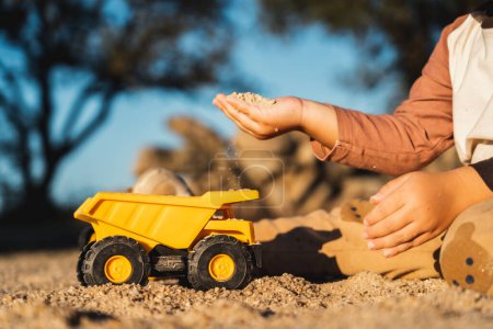 Foto de Buen niño feliz jugando con la máquina excavadora y el camión bajo la luz del sol - Imagen libre de derechos