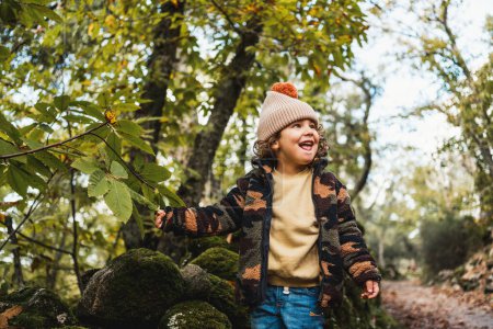 Foto de Retrato de niño de moda con sombrero jugando felizmente en un sendero forestal mientras enseñaba a sus padres sobre las plantas - Imagen libre de derechos