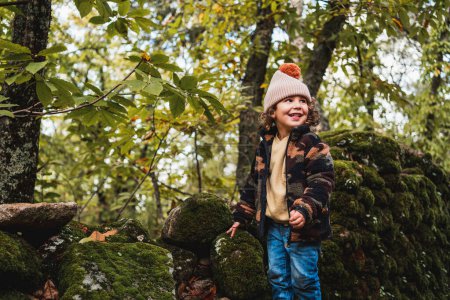 Téléchargez les photos : Portrait de petit garçon à la mode avec chapeau jouant joyeusement sur un chemin de forêt tout en enseignant à ses parents sur les plantes - en image libre de droit