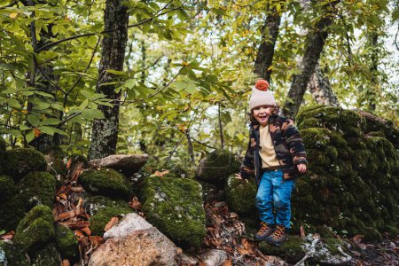 Téléchargez les photos : Portrait de petit garçon à la mode avec chapeau jouant joyeusement sur un chemin de forêt tout en enseignant à ses parents sur les plantes - en image libre de droit