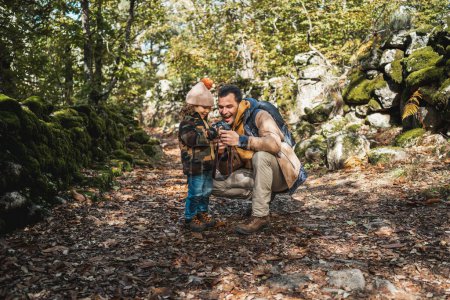 Photo for Photographer father and his fashionable son happy watching photographs on the photo camera in a beautiful environment - Royalty Free Image