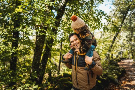 Foto de Fotógrafo padre y su hijo de moda con un sombrero en los hombros, feliz, caminando a través de un entorno hermoso - Imagen libre de derechos