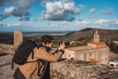 Foto de Retrato del joven fotógrafo, fotografiando una ciudad que viaja con su mochila y cámara de turismo, visto desde el lado - Imagen libre de derechos