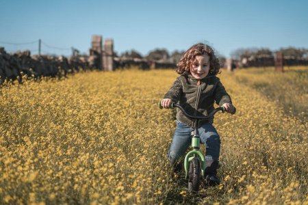 Foto de Niño feliz y alegre jugando con la bicicleta en un prado de flores amarillas en el día soleado y el cielo azul - Imagen libre de derechos