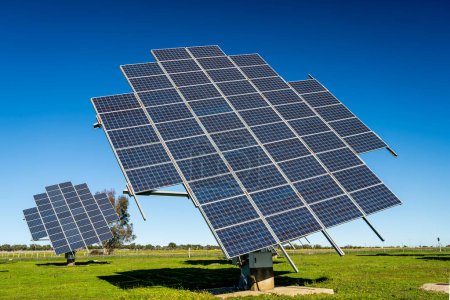 Foto de Conjunto de paneles solares móviles en la producción de energía eléctrica fotovoltaica parque solar sobre prado verde en día soleado brillante - Imagen libre de derechos