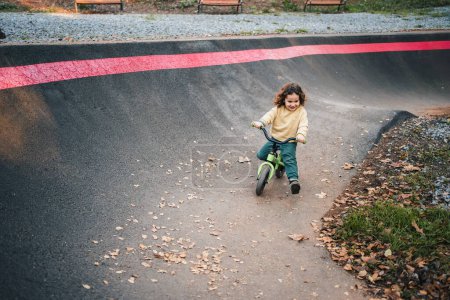 Téléchargez les photos : Heureux petit garçon pratiquant avec son vélo sur circuit de piste de pompe - en image libre de droit
