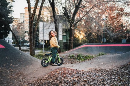 Téléchargez les photos : Petit garçon à la mode plaisantant avec son vélo sur circuit de piste de pompe - en image libre de droit