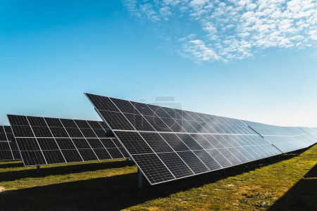 Foto de Paneles solares en pradera verde y cielo azul, en planta solar fotovoltaica, día soleado brillante - Imagen libre de derechos