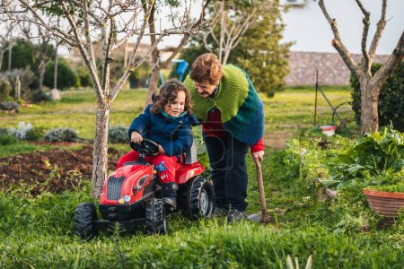Téléchargez les photos : Grand-mère et petit-fils jouant avec un tracteur dans le jardin à la maison - en image libre de droit