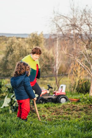 Téléchargez les photos : Petit garçon observant le jardin avec sa grand-mère, l'aidant avec le travail - en image libre de droit