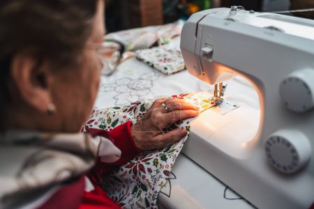 Photo for Senior woman in red sewing a garment with sewing machine - Royalty Free Image