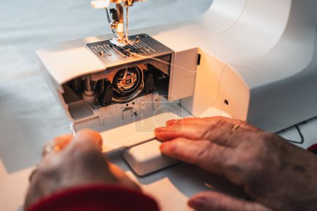 Foto de Detalle de los dedos de costurera preparando la máquina de coser para trabajar y coser con ella - Imagen libre de derechos