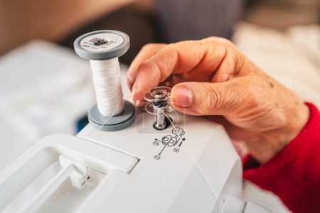 Photo for Detail of senior woman hands preparing bobbin of thread on sewing machine - Royalty Free Image
