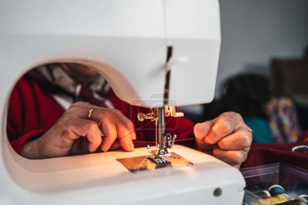 detalle de la mano de costurera con hilos entre los dedos junto a la máquina de coser