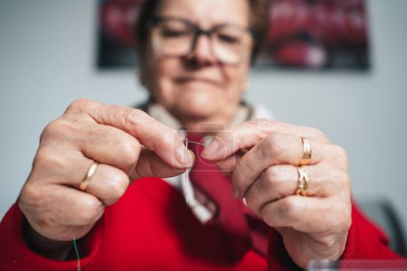 Foto de Costurera concentrada con gafas que roscan el hilo de coser en la aguja - Imagen libre de derechos