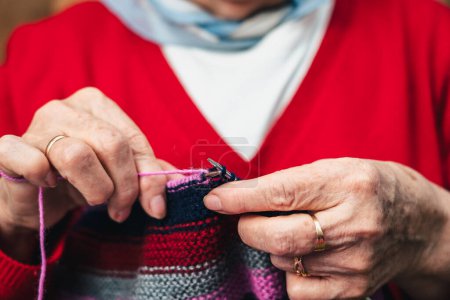 Foto de Detalle de las manos de la costurera mujer mayor costura ropa hecha a mano con lana de colores de punto - Imagen libre de derechos