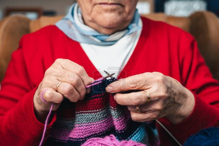 Photo for Detail of hands of senior woman seamstress sewing handmade clothes with colorful wool knit - Royalty Free Image