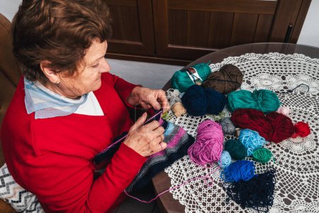Foto de Foto horizontal de la mujer mayor tejiendo con lana y agujas sentado en la sala de estar en casa - Imagen libre de derechos