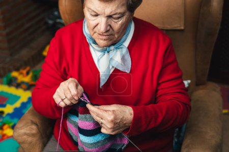 Photo for Horizontal low angle portrait of senior woman sewing with wool on the sofa at home happy doing craft activity - Royalty Free Image