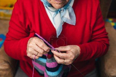 Photo for Horizontal and overhead portrait of senior woman's hands sewing with wool on the sofa at home happy doing craft activity - Royalty Free Image
