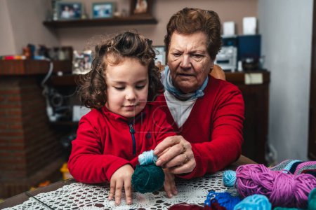 Téléchargez les photos : Portrait de grand-mère et petit-fils heureux jouant avec de la laine à coudre à la maison lui apprenant à coudre - en image libre de droit