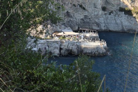 Téléchargez les photos : Marina del Cantone - 4 septembre 2023 : Restaurant Conca del Sogno, avec hôtel attenant et lido, dans la baie de Recommone au coucher du soleil - en image libre de droit