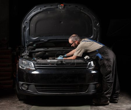 Foto de Vista frontal de un mecánico reparando un coche negro. concepto de reparaciones del hogar. - Imagen libre de derechos
