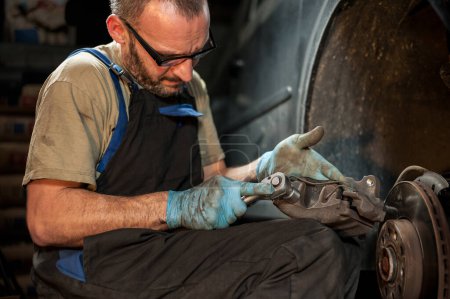 Téléchargez les photos : Un homme dans un atelier sombre desserrant un boulon sur sa voiture. Concept de réparations domiciliaires. - en image libre de droit