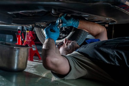 Foto de Un hombre bajo un coche cambiando aceite. concepto de reparaciones del hogar. - Imagen libre de derechos
