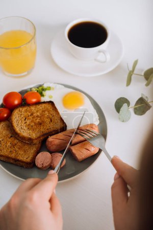 Foto de Desayuno inglés con café negro y zumo de naranja, salchichas a la parrilla y tostadas de trigo integral con huevo frito y tomates cherry en el plato - Imagen libre de derechos