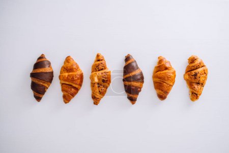 Foto de Colocación plana de varios deliciosos croissants marrones y chocolate dispuestos en una línea sobre una mesa blanca - Imagen libre de derechos