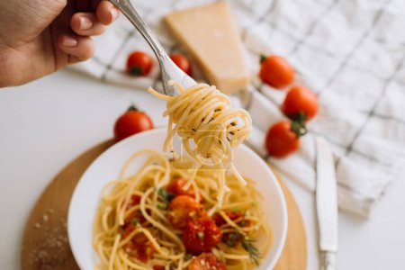 Foto de Espaguetis envueltos en tenedor en el fondo de una porción de pasta con tomates cherry en un plato y queso parmesano - Imagen libre de derechos