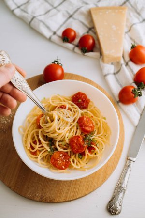 Foto de Porción de pasta de espaguetis con parmesano y tomates cherry espolvoreados con especias en un plato sobre tabla de madera - Imagen libre de derechos