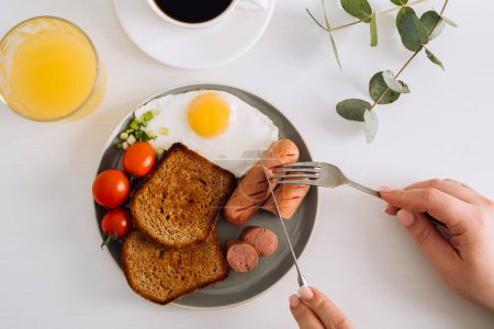 Foto de Desayuno inglés con café negro y zumo de naranja, salchichas a la parrilla y tostadas de trigo integral con huevo frito y tomates cherry en el plato - Imagen libre de derechos