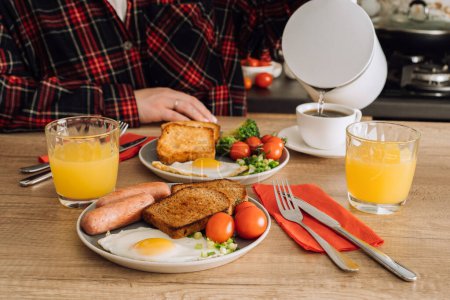 Foto de Mujer irreconocible vierte agua en la taza, se prepara para disfrutar de un desayuno inglés con café y jugo de naranja en la cocina - Imagen libre de derechos