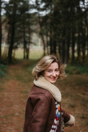 Foto de Feliz y alegre mujer caucásica adulta en una chaqueta marrón está caminando a través del bosque de otoño - Imagen libre de derechos