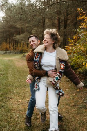 Foto de Pareja feliz se divierte en medio del bosque, hombre sonriente abrazando a su novia en un parque de otoño - Imagen libre de derechos