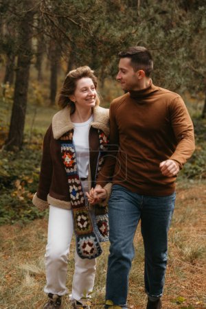 Foto de Feliz hombre y mujer están caminando a través del bosque de otoño, tomados de la mano, pareja adulta pasar tiempo juntos al aire libre - Imagen libre de derechos
