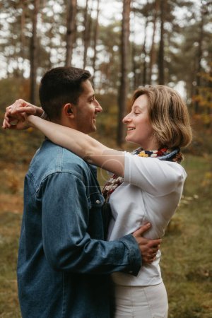 Foto de Feliz hombre y mujer se abrazan en el bosque en otoño, sonriendo felizmente con sus brazos envueltos uno alrededor del otro - Imagen libre de derechos