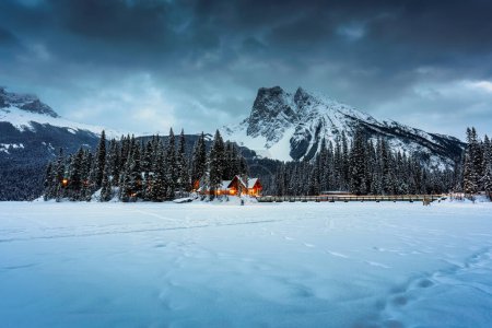Beautiful view of Emerald Lake with wooden lodge glowing in snowy pine forest and rocky mountains on winter at Yoho national park, Alberta, Canada