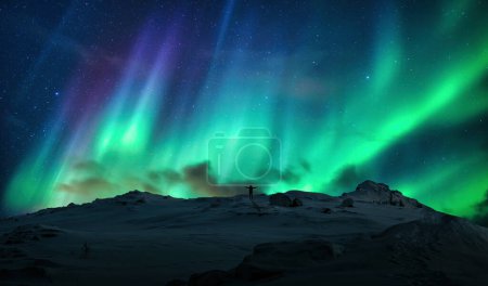 Foto de Fantástica Aurora boreal, auroras boreales sobre silueta hombre alegre en la cima de la montaña en círculo ártico en Noruega - Imagen libre de derechos