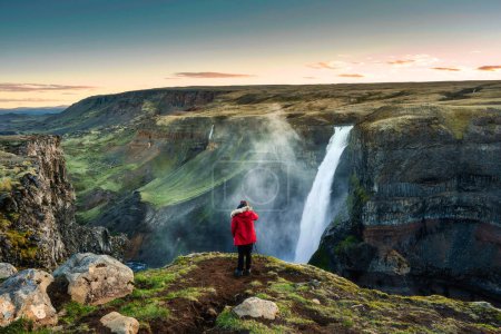 Téléchargez les photos : Majestueuse cascade de Haifoss coulant dans le canyon volcanique et voyageur prenant une photo parmi les Highlands islandais en été en Islande - en image libre de droit