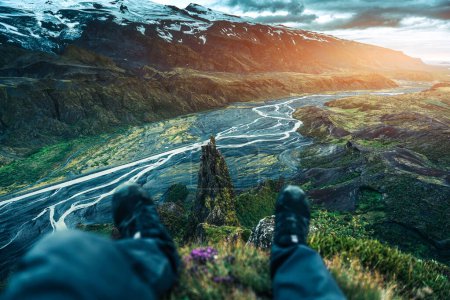 Punto de vista del viajero masculino sentado en el mirador de Valahnukur de la montaña volcánica y el río glaciar durante el verano en las tierras altas de Islandia en Thorsmork, Islandia