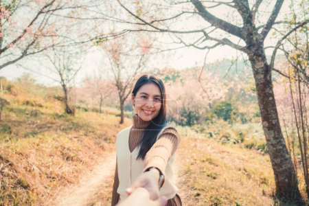 Happy young asian woman holding hands with her boyfriend enjoying in wild himalayan cherry blooming in springtime at Phu Lom Lo 