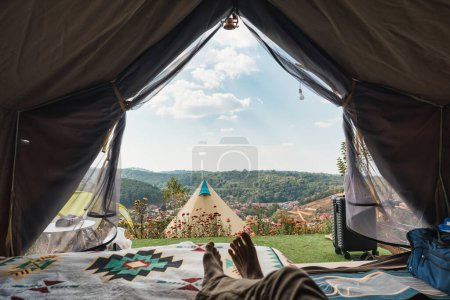 Male traveler relaxing and enjoying with the mountain, local village view inside camping tent on vacation at Thailand. POV Shot