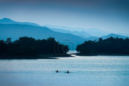 Foto de Colorida escena azul del embalse Kaeng Krachan con barco pesquero y canoa de remos turística en Phetchaburi, Tailandia - Imagen libre de derechos