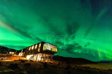 Hermosa vista panorámica de Aurora boreal, luces boreales que brillan sobre un hotel de lujo en el monte Hengill en invierno en Nesjavellir, Islandia